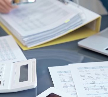 Person using a calculator on a desk filled with financial papers and a laptop nearby.